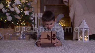 一个小男孩打开一个带礼物的盒子，高兴地躺在圣诞树附近的地板上。 高清高清
